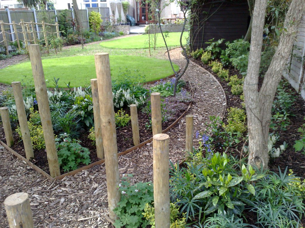 View of garden looking back to the house from the softwood post crossroad feature with elder tree and groundcover evergreen shrubs lining the curving paths out